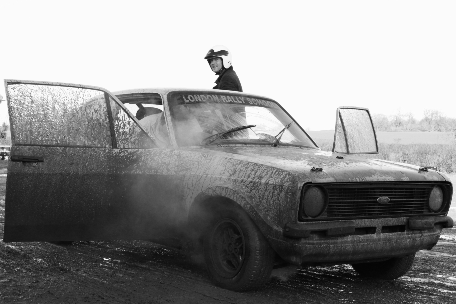 Sam White in a crash helmet stepping out of a muddy racing car