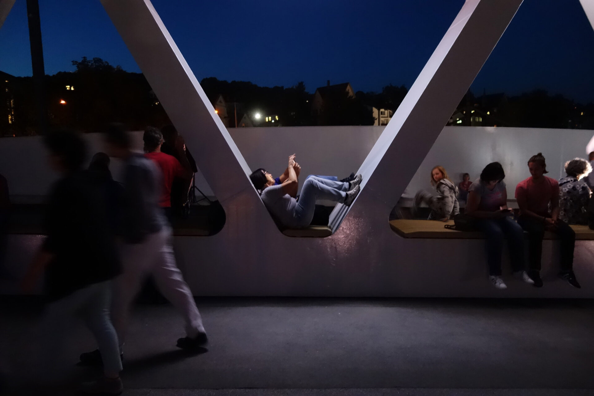 Two people sitting in archway of bridge central seating area looking at phone at night