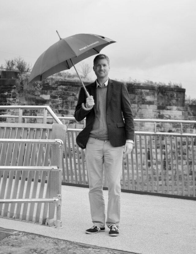 Sam White in a dark jacket holding an umbrella