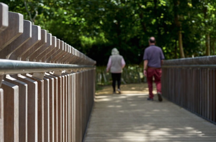 Close view of the handrail and parapet of the footbridge with people walking off the bridge in the distance