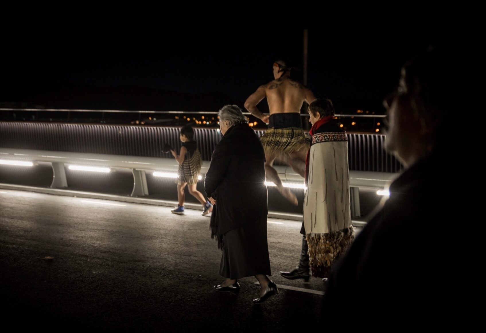 Maori people at opening ceremony walking across the deck at night with bridge lighting