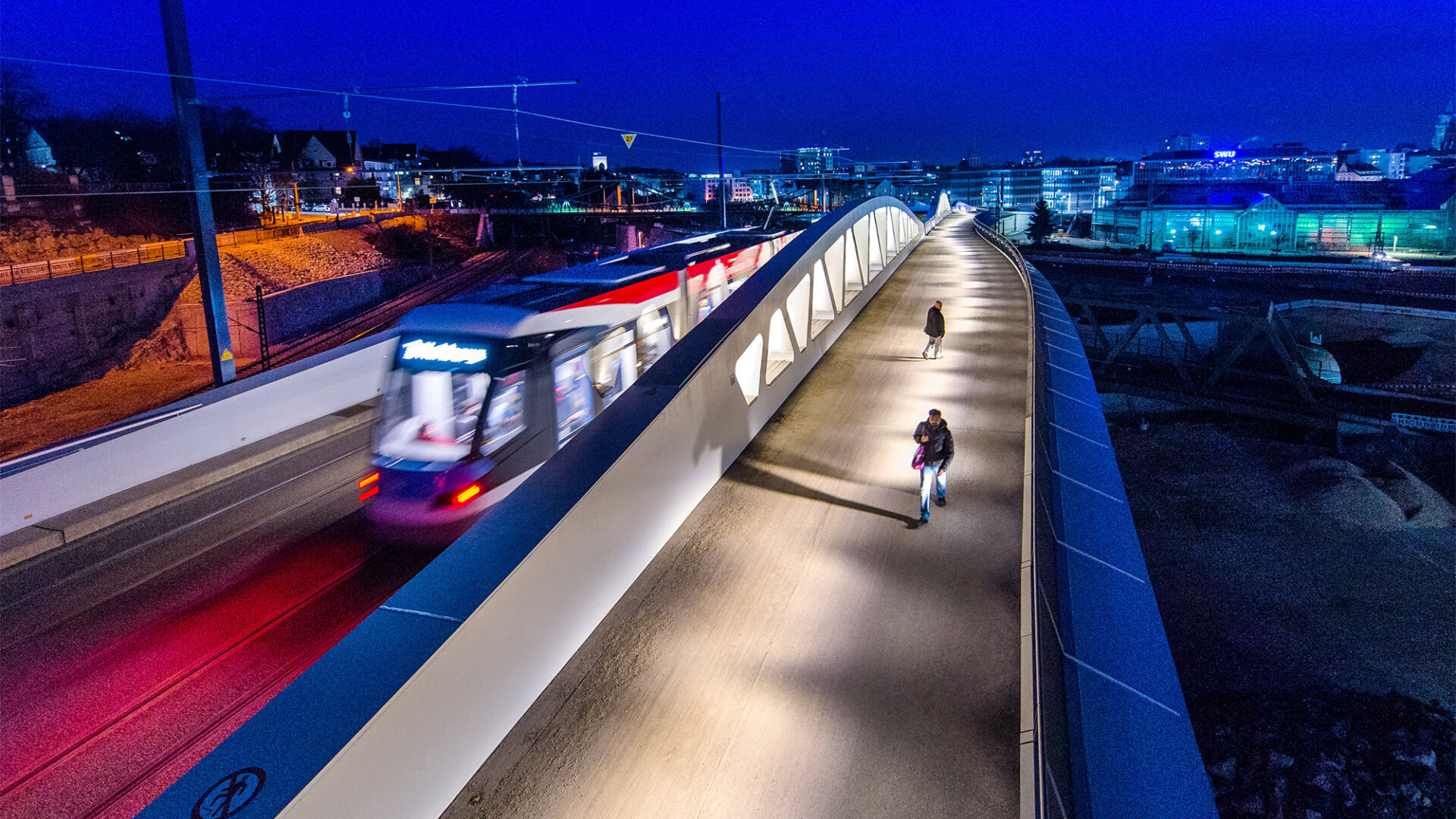 Straßenbahn und Fußgängerbrücke über Eisenbahnschienen bei Nacht